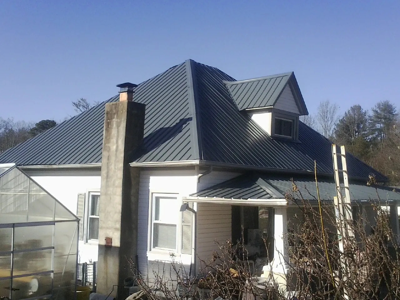 Dark blue standing seam metal roof on a white farmhouse with dormer — Slate & Tile Roof Repair by Roofing Brothers in Emery