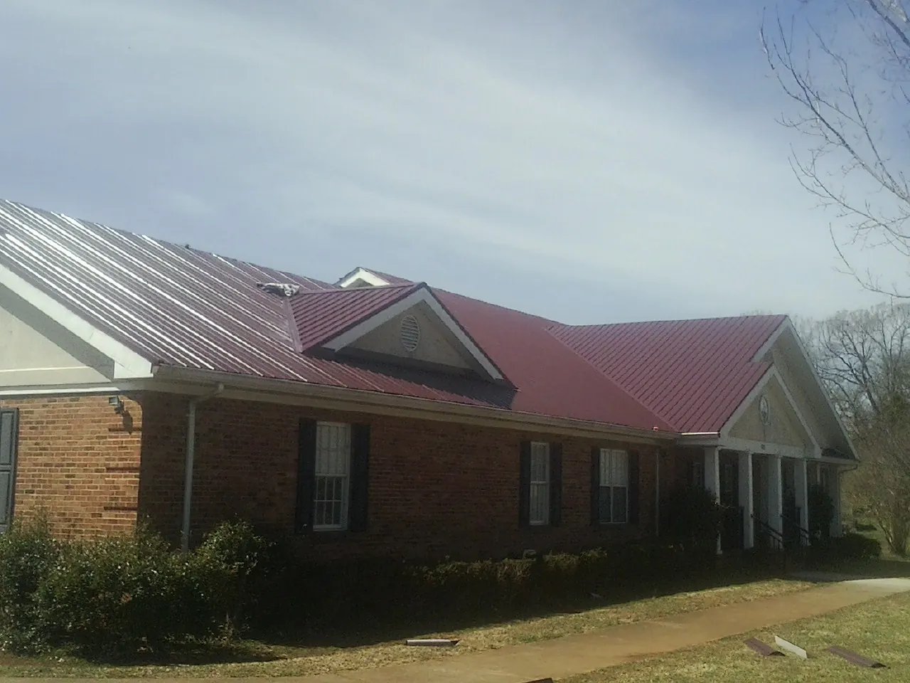 Red metal roof with gabled entries on a long brick building, from a Hail Damage Roof Repair job in Emery