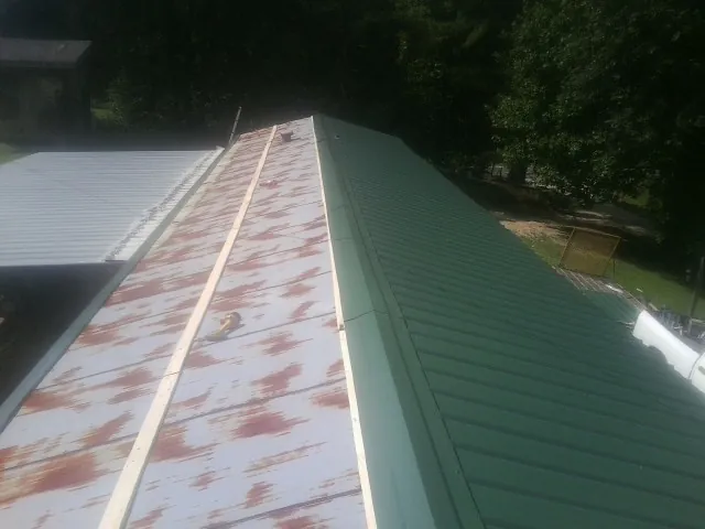 Old rusted panels beside newly installed green metal roofing — Wind Damage Roof Repair by Roofing Brothers in Emery