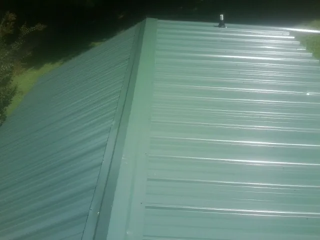 New green metal panels meeting at the ridge of a roof — Flat Roof Repair work by our crew in Emery
