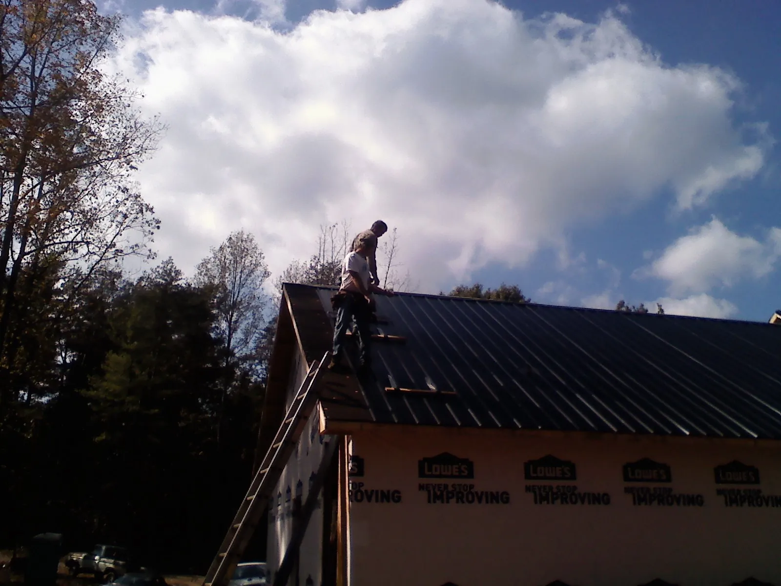Roofer fastening dark metal panels high against a cloudy sky, from a Roof Inspection job in Emery